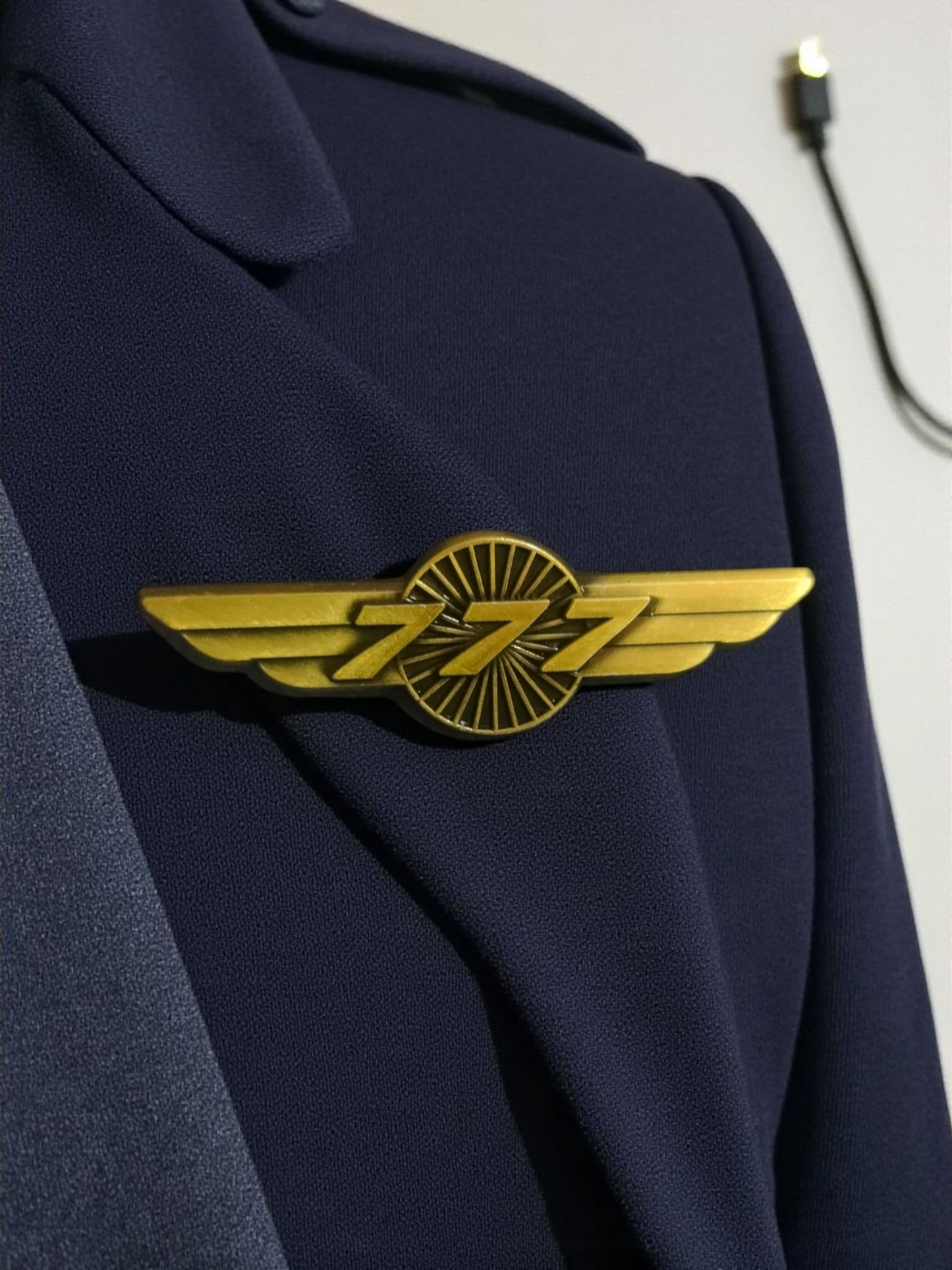 Gold Boeing 777 wing pin on a fabric background, symbolizing aviation and pilot recognition